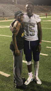 Deyon Bouie in a football uniform, standing on a football field, with one arm around a family member
